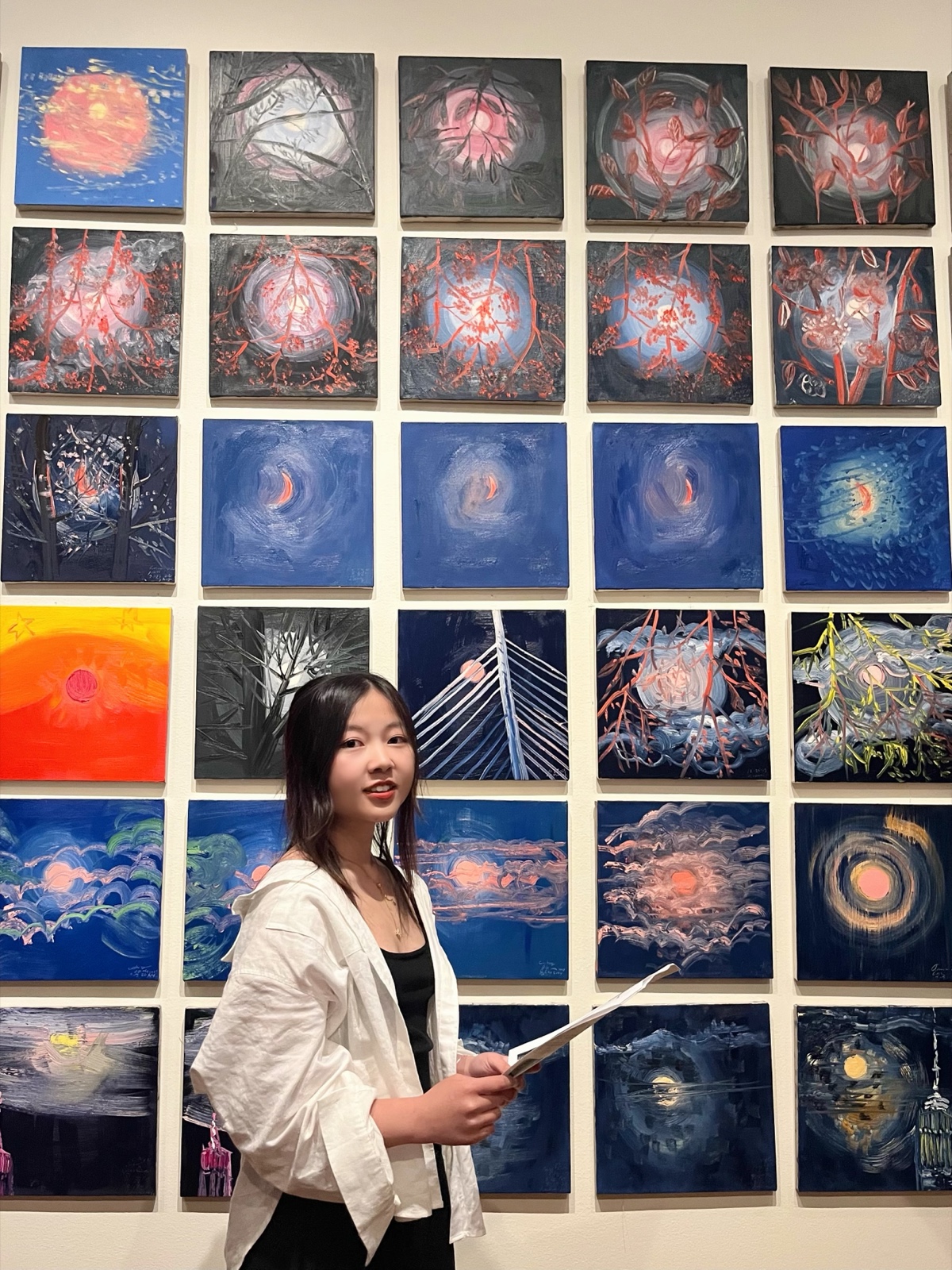 Xingyue at a gallery installation, in front of a wall of paintings